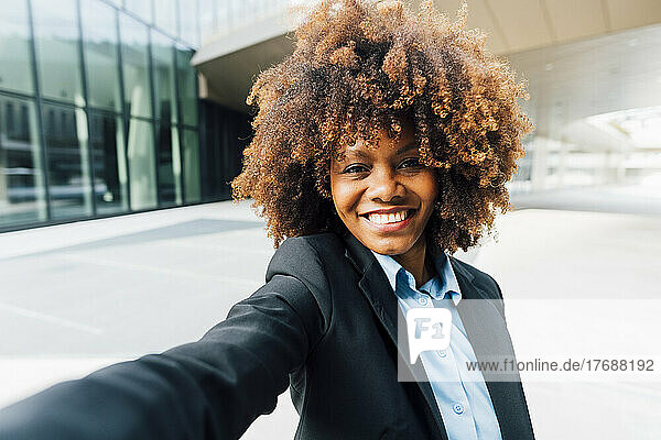 Smiling Afro businesswoman taking selfie standing outside office building