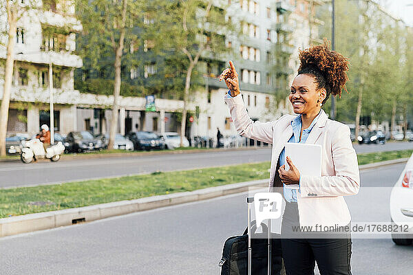 Smiling businesswoman holding tablet PC hitchhiking at roadside