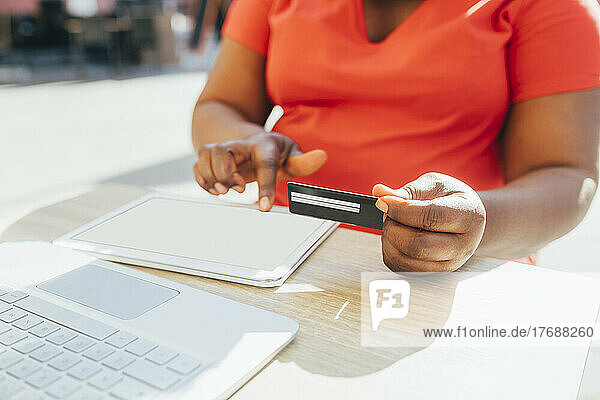 Mature woman holding credit card doing online shopping though tablet PC on sunny day