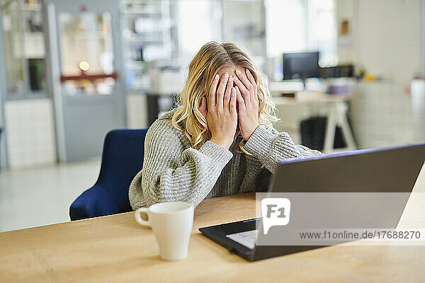 Despaired young woman sitting at desk in office with laptop
