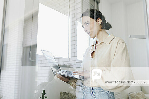Junge Frau mit Laptop schaut durchs Fenster