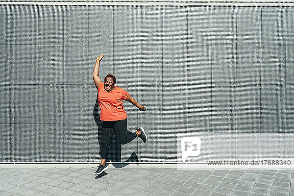 Happy mature woman jumping in front of wall