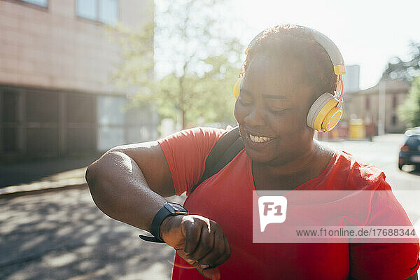 Glückliche Frau  die Musik hört und die Zeit auf einer Smartwatch überprüft