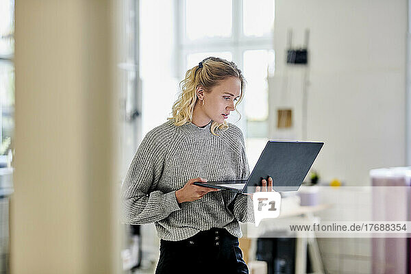 Junge Frau steht mit Laptop im Büro
