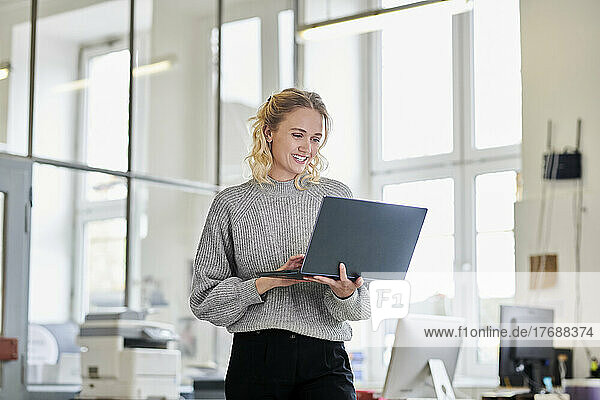 Glückliche junge Frau  die im Büro steht und einen Laptop benutzt