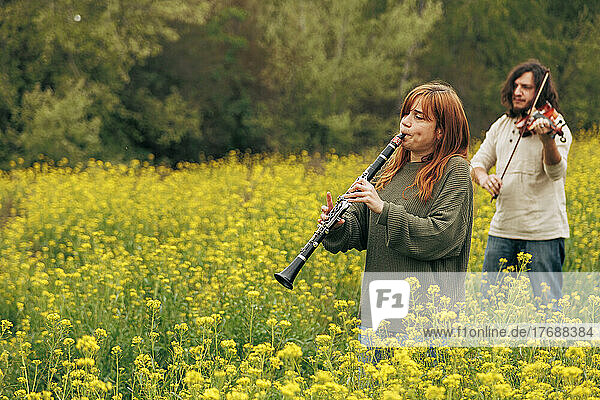 Woman practicing clarinet with man playing violin walking in flower field