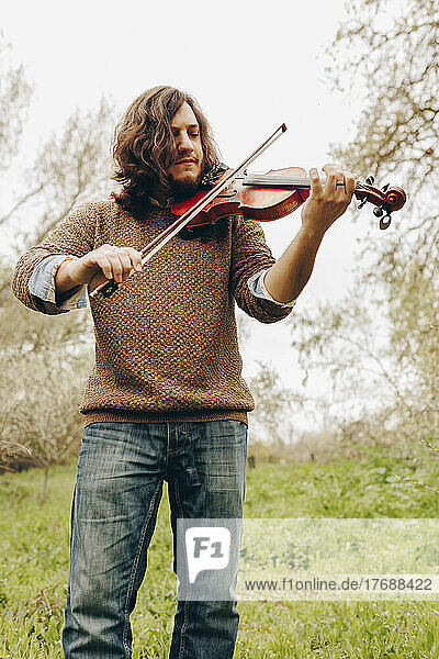 Man with long hair playing violin standing in field