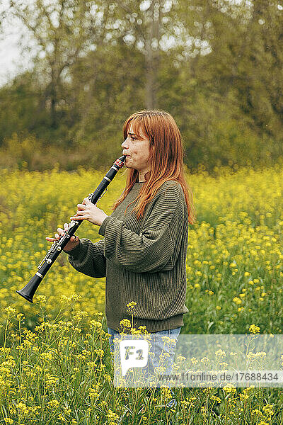 Redhead woman practicing clarinet standing in flower field