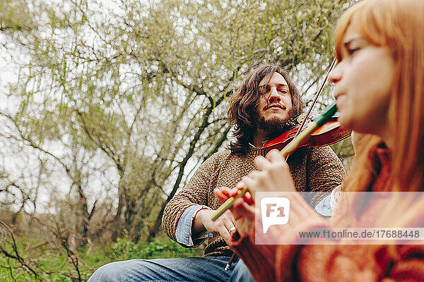 Konzentrierter Mann spielt Geige mit Frau im Feld