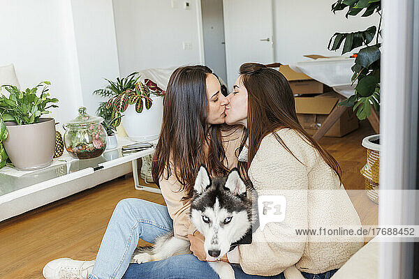 Lesbian couple kissing each other sitting with dog in apartment