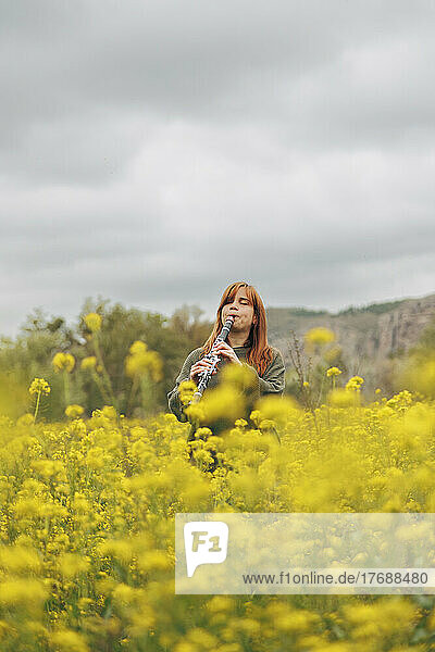 Woman playing clarinet standing in flower field