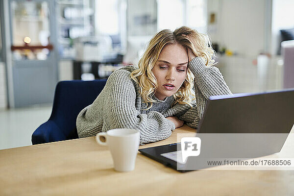 Tired young woman sitting at desk in office with laptop