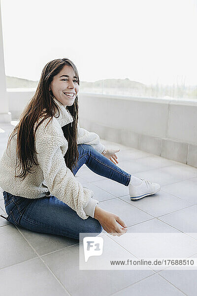 Glückliche junge Frau mit langen Haaren sitzt auf der Terrasse