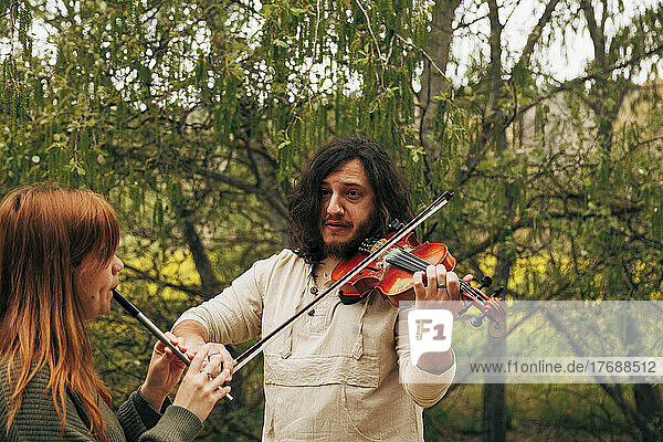 Man practicing violin looking at woman playing tin whistle