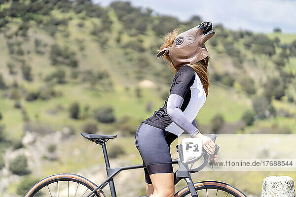 Cyclist with bicycle wearing horse mask on sunny day