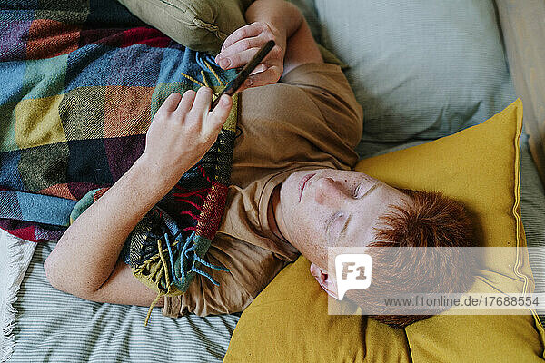 Teenage boy using smart phone lying on bed in bedroom
