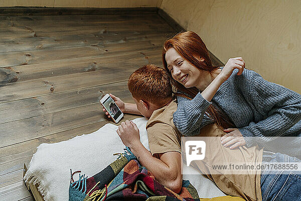 Boy holding mobile phone lying on floor with girlfriend at weekend