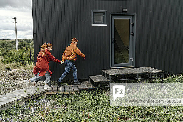 Junges Paar hält sich an den Händen und rennt gemeinsam auf ein kleines Haus zu