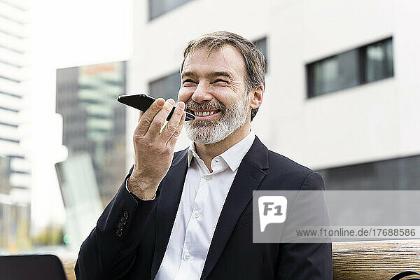 Happy businessman sending voicemail through smart phone