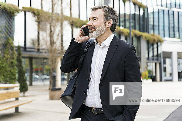 Businessman talking on smart phone standing outside office building