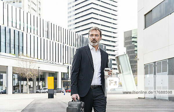 Businessman with laptop bag and disposable coffee cup standing outside office building