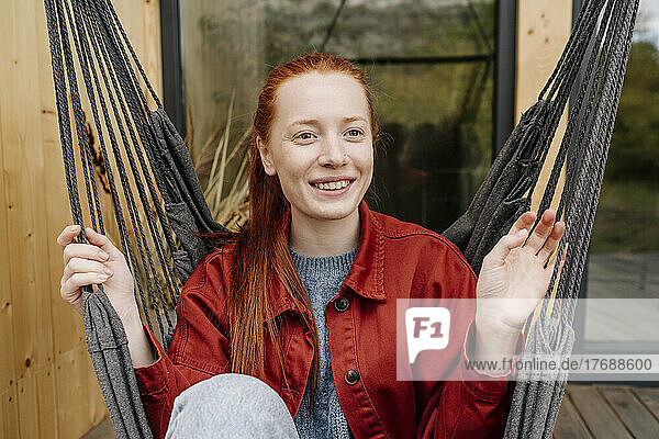 Smiling woman in hanging hammock chair at deck