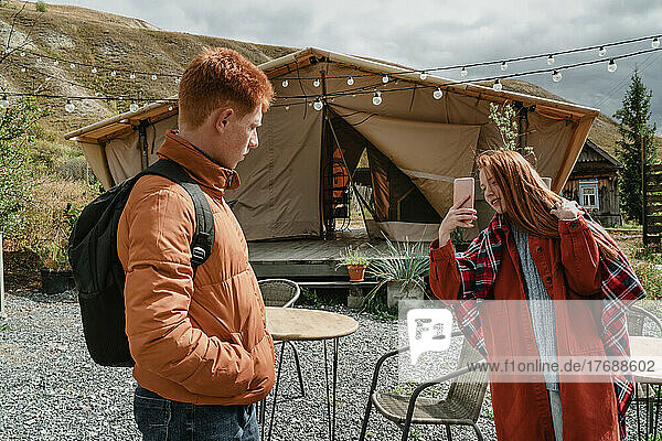 Young woman photographing boyfriend through smart phone by glamping tent