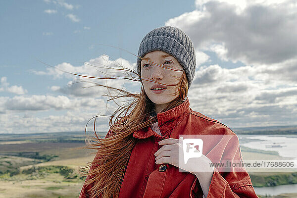 Young woman with knit hat standing under cloudy sky