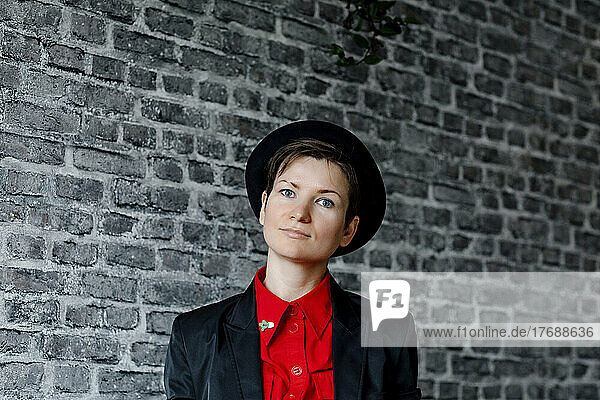 Smiling woman wearing hat standing in front of brick wall