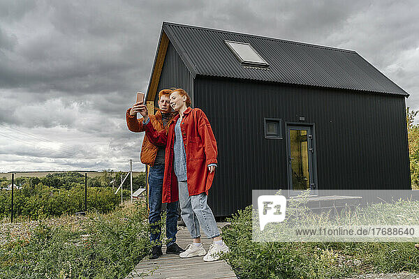 Young couple taking selfie standing in front of tiny house