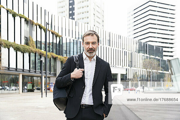 Smiling businessman with hand in pocket standing in front of modern office building