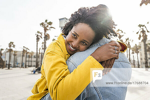 Happy woman with Afro hairstyle hugging man on sunny day