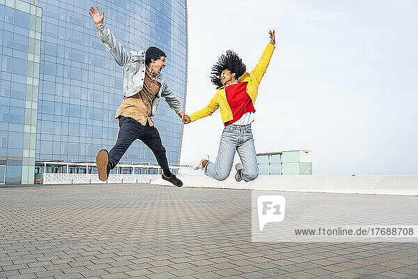 Happy couple with hands raised jumping on footpath