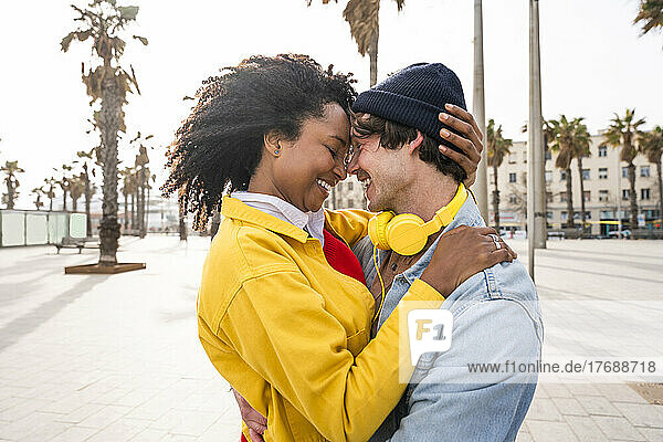 Smiling woman with Afro hairstyle embracing man on footpath
