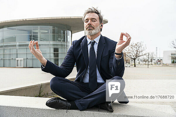 Mature businessman with eyes closed meditating sitting on wall