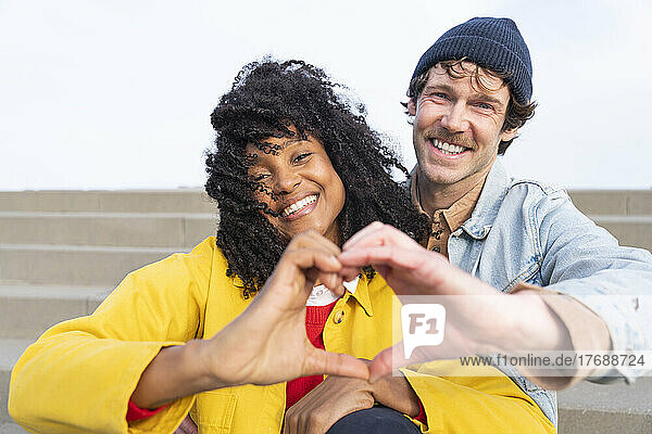 Happy couple gesturing heart shape sitting together on steps