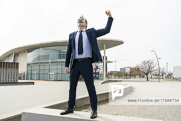 Businessman flexing muscles standing on wall at office park