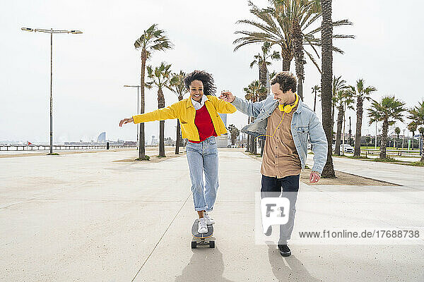 Happy man teaching skateboarding to woman on footpath