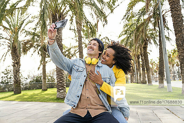 Glücklicher Mann macht Selfie mit Freundin per Smartphone im öffentlichen Park