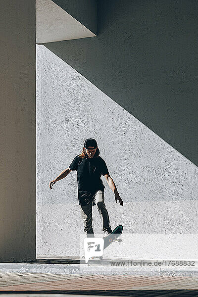 Mann fährt an sonnigem Tag vor der Wand Skateboard