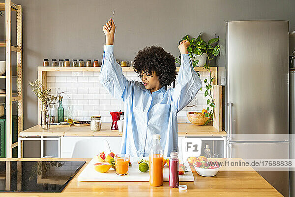 Happy woman with arms raised dancing in kitchen at home