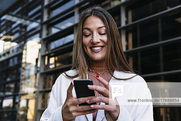 Happy businesswoman using smart phone at office building