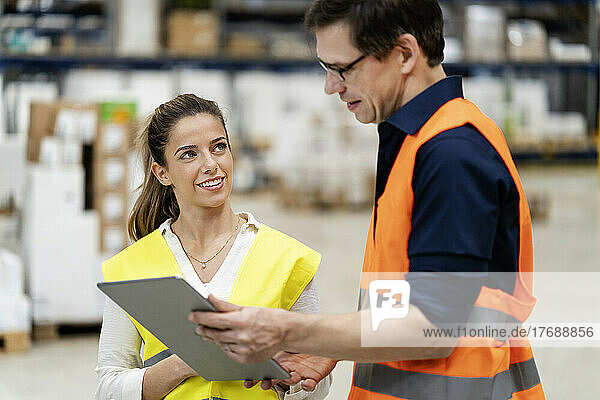 Young blue-collar discussing with colleague over tablet PC at factory