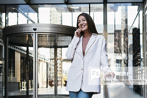 Happy businesswoman talking on mobile phone at office building