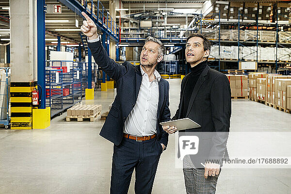 Mature businessman pointing and discussing with colleague in meeting at warehouse