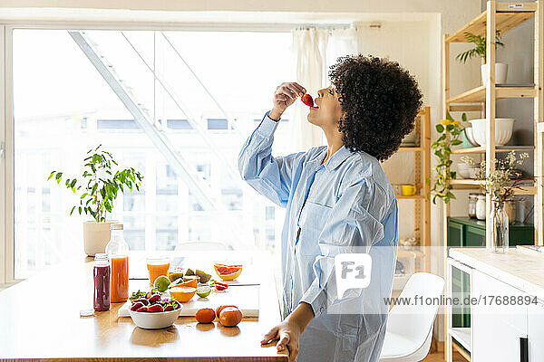Young woman eating strawberry in kitchen at home