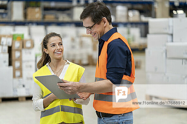 Smiling blue-collar workers discussing over tablet computer in warehouse