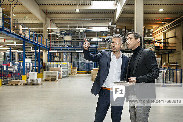 Businessman discussing with colleague holding tablet PC in factory