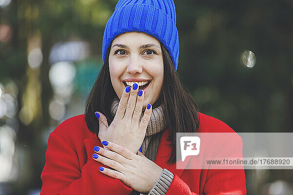 Überraschen Sie junge Frau mit blauem Nagellack  der den Mund mit der Hand bedeckt