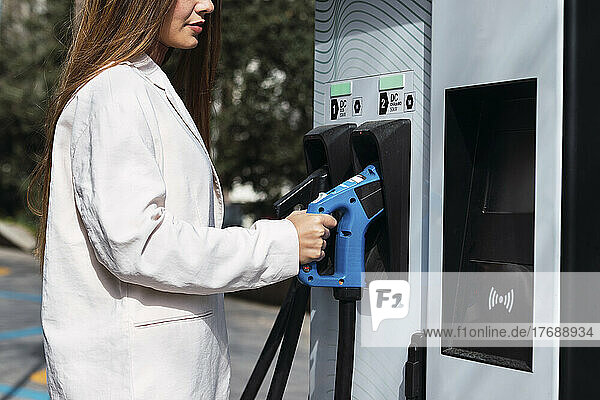 Woman holding electric plug at charging station